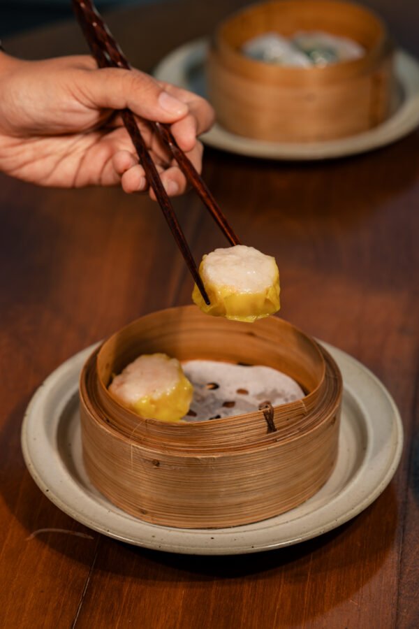 Chopsticks lifting a dim sum dumpling above a bamboo basket at Tree O’Clock Phuket